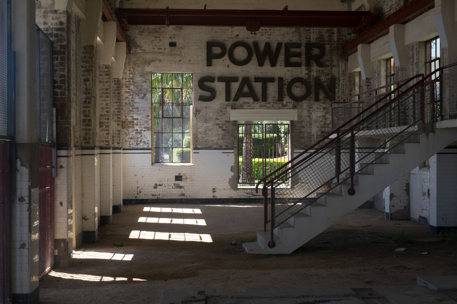 Darkened run down space with white and white washed brick walls staircase leading to right of the image and the words Power Station set onto the wall